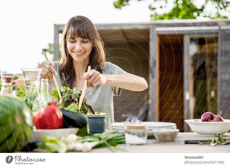 Smiling woman preparing a salad on garden table human human being human beings humans person persons celibate celibates singles solitary people solitary person
