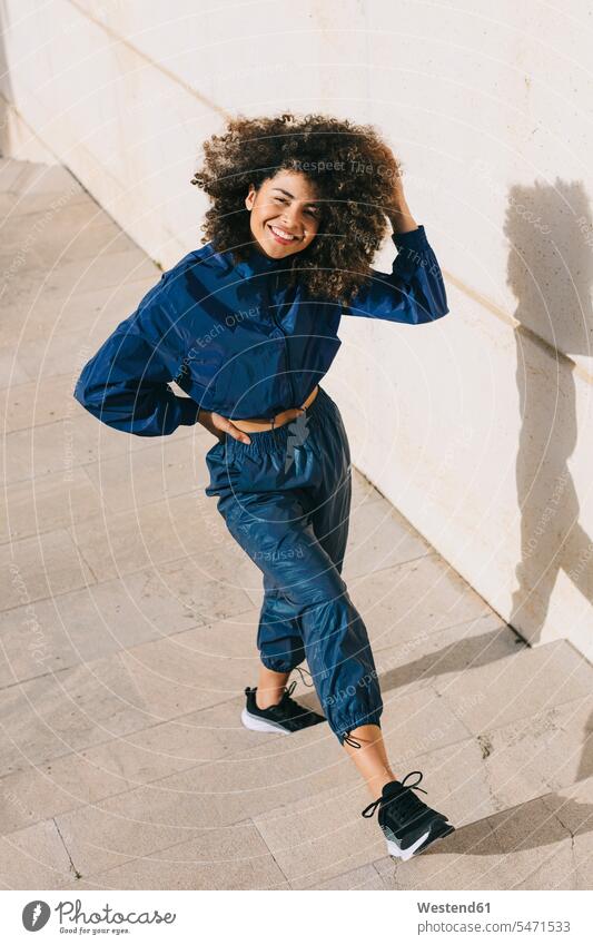 Portrait of happy stylish young woman wearing tracksuit outdoors human human being human beings humans person persons curl curled curls curly hair smile delight