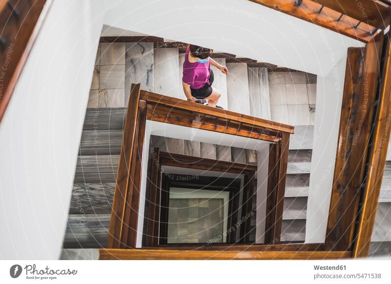 Young woman wearing face mask looking up while standing on spiral staircase color image colour image indoors indoor shot indoor shots interior interior view