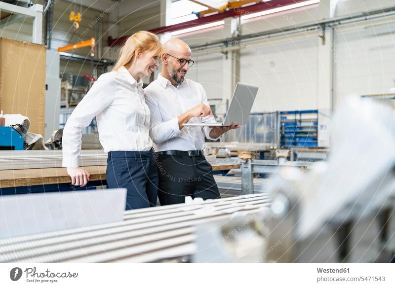 Smiling businessman and businesswoman using laptop in factory factories smiling smile businesswomen business woman business women Businessman Business man
