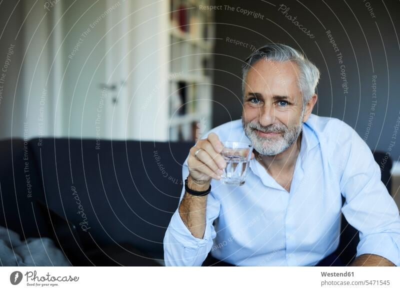 Smiling mature man drinking glass of water on the sofa at home human human being human beings humans person persons celibate celibates singles solitary people