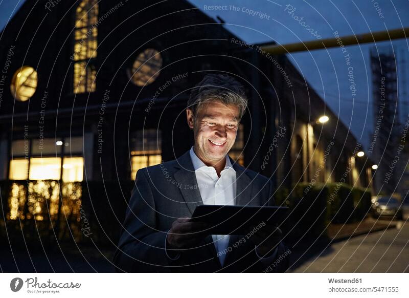 Smiling businessman using tablet outside modern building at night by night nite night photography buildings smiling smile digitizer Tablet Computer Tablet PC