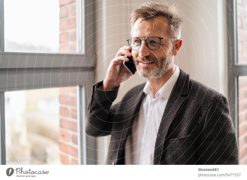 Businessman on cell phone at the window in office offices office room office rooms Business man Businessmen Business men mobile phone mobiles mobile phones