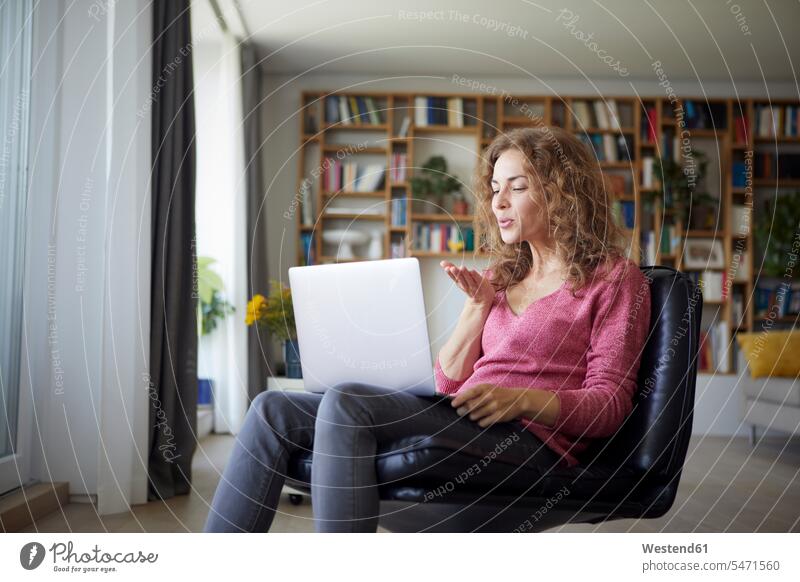 Woman blowing kiss to video call on laptop while sitting at home color image colour image indoors indoor shot indoor shots interior interior view Interiors day