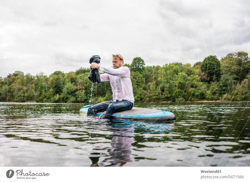 Wet businessman sitting on SUP board on a lake business life business world business person businesspeople Business man Business men Businessmen Seated solitary