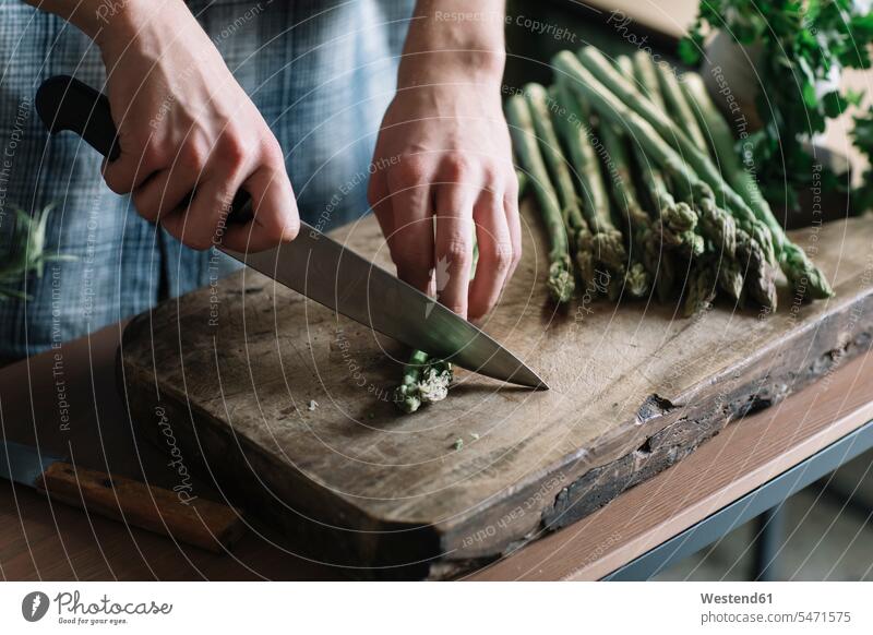 Hands of man cutting fresh asparagus on board in kitchen color image colour image indoors indoor shot indoor shots interior interior view Interiors day