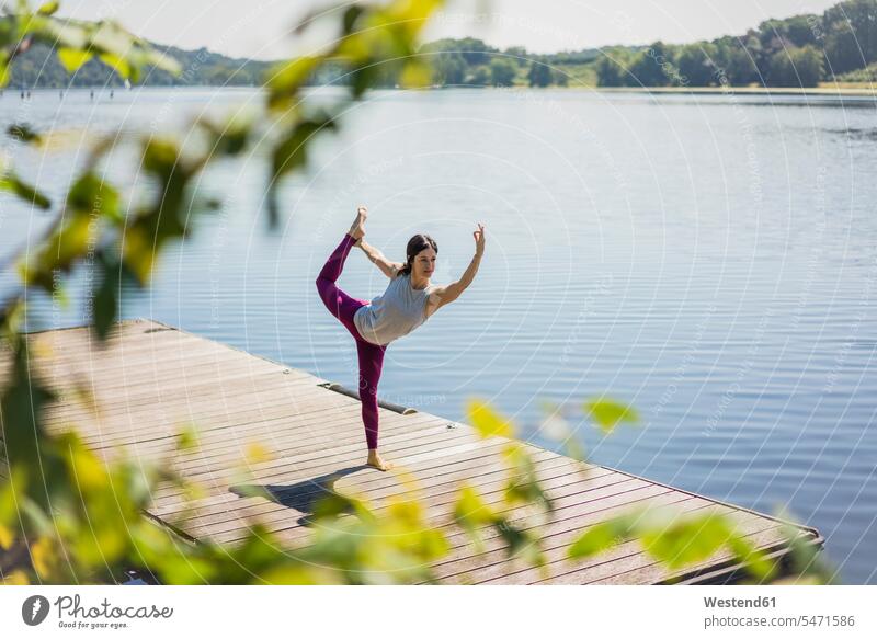Mature woman practicing yoga in summer on a jetty at a lake Yoga lakes summer time summery summertime jetties practice practise exercise exercising practising
