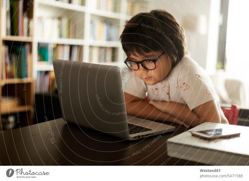 Cute boy with eyeglasses using laptop while sitting at table in living room color image colour image indoors indoor shot indoor shots interior interior view