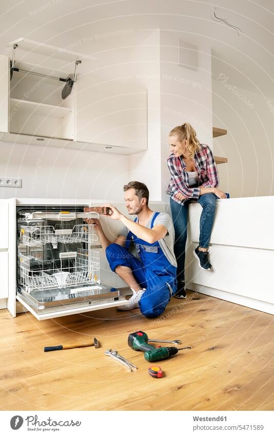 Couple fitting dishwasher in their new built-in kitchen Fitting domestic kitchen kitchens fitted kitchen assembling installing Spirit Level watching observing