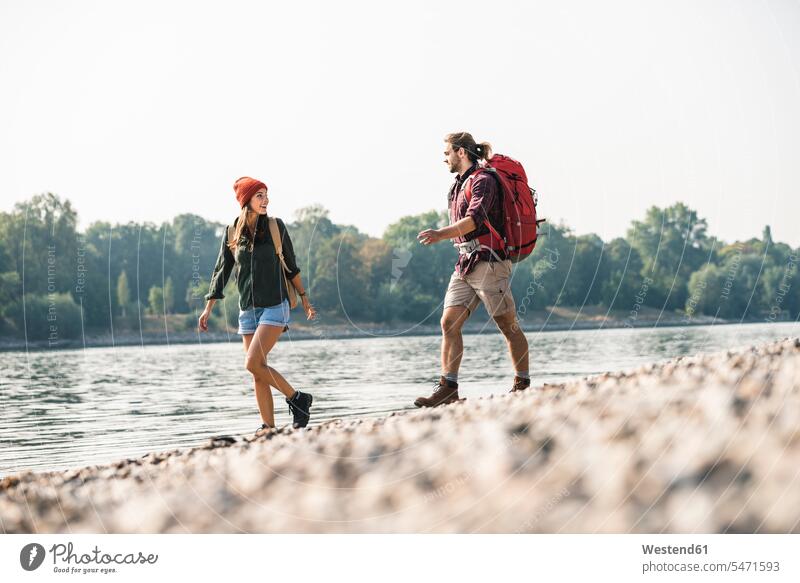 Young couple with backpacks walking at the riverside rucksacks back-packs River Rivers riverbank twosomes partnership couples going water waters body of water