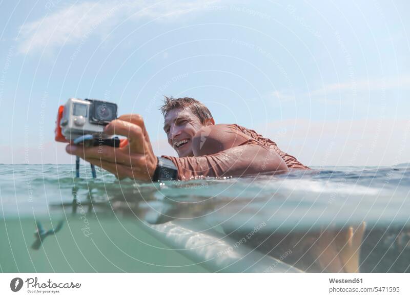 Surfer with action camera lying on surfboard sports aquatics Water Sport surf ride surf riding Surfboarding surf board surf boards surfboards cameras smile