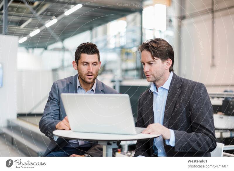 Two businessmen sharing laptop in factory Laptop Computers laptops notebook Businessman Business man Businessmen Business men modern contemporary factories