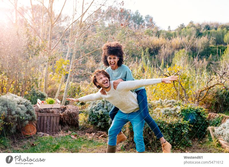 Man carrying girlfriend piggyback in a garden in the countryside playing carefree messing about silly silliness piggy-back pickaback Piggybacking Piggy Back