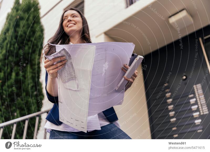 Happy woman with face mask and blue print in hand looking at outside area of house Occupation Work job jobs profession professional occupation business life