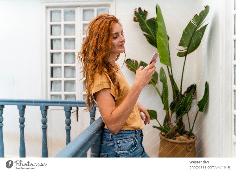 Smiling redheaded young woman leaning against railing looking at cell phone T- Shirt t-shirts tee-shirt telecommunication phones telephone telephones