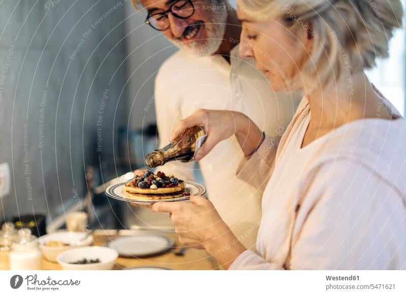 Mature couple preparing pancakes in kitchen at home dish dishes Plates hold smile in the morning delight enjoyment Pleasant pleasure happy Contented Emotion