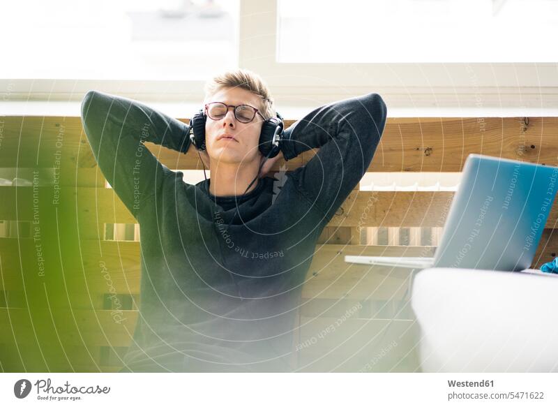 Relaxed young man sitting on the floor listening to music with headphones men males relaxed relaxation Seated laptop Laptop Computers laptops notebook headset