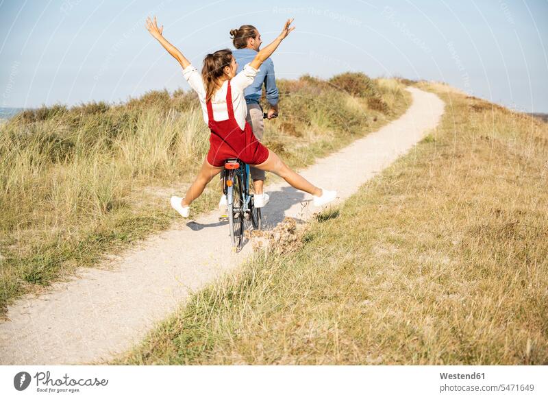Carefree girlfriend enjoying bicycle ride with boyfriend on sunny day color image colour image outdoors location shots outdoor shot outdoor shots daylight shot