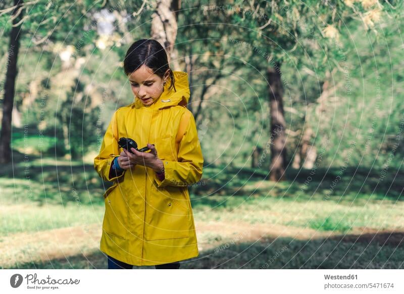 Girl wearing yellow raincoat in nature looking at compass compasses navigational compass natural world girl females girls eyeing standing measuring device