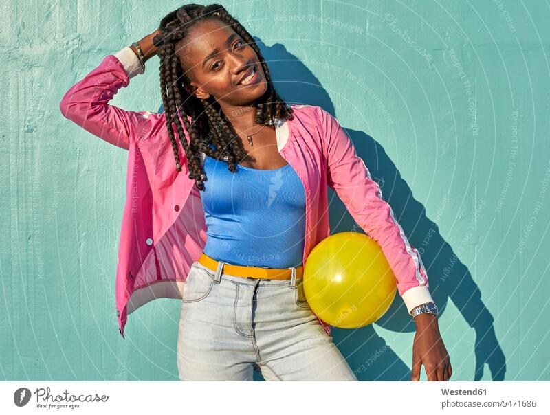 Young black woman with a yellow ball in front of a blue wall coat coats jackets balls hold smile play delight enjoyment Pleasant pleasure happy Emotions Feeling