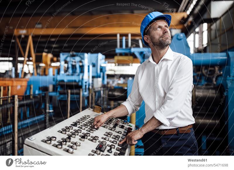 Male entrepreneur operating control panel looking up while standing at industry color image colour image indoors indoor shot indoor shots interior interior view
