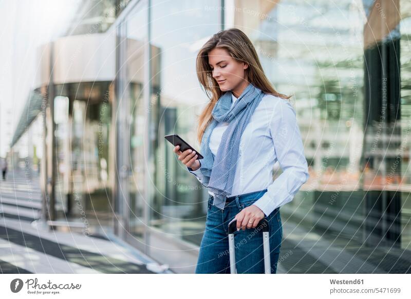 Young businesswoman with suitcase looking at smartphone businesswomen business woman business women suitcases watching Smartphone iPhone Smartphones