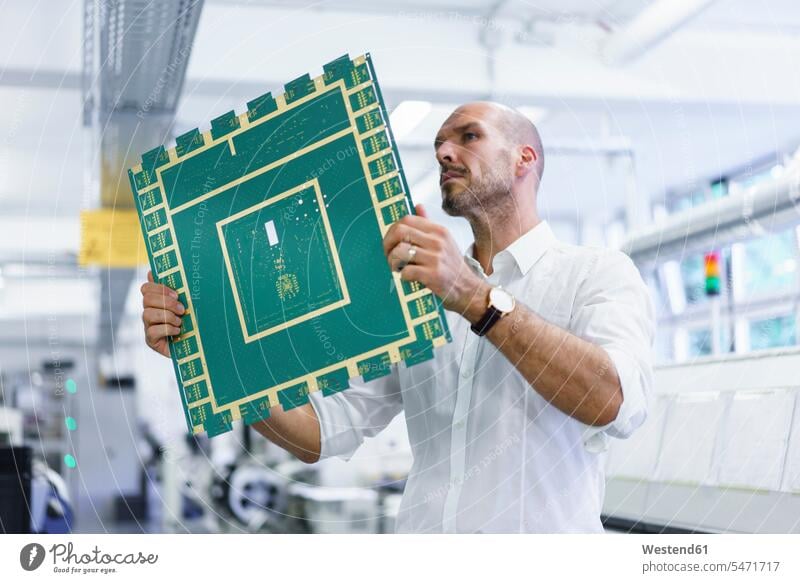 Confident mature male technician looking at large circuit board while examining in illuminated factory color image colour image indoors indoor shot indoor shots