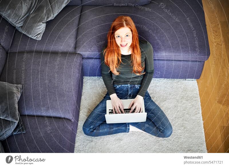 Redheaded woman sitting on floor in the living room using laptop females women Laptop Computers laptops notebook Seated redheaded red hair red hairs red-haired