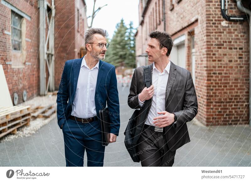 Two businessmen walking and talking at an old brick building brick buildings speaking going 25-30 years 25 to 30 25 to 30 years discussing discussion executive