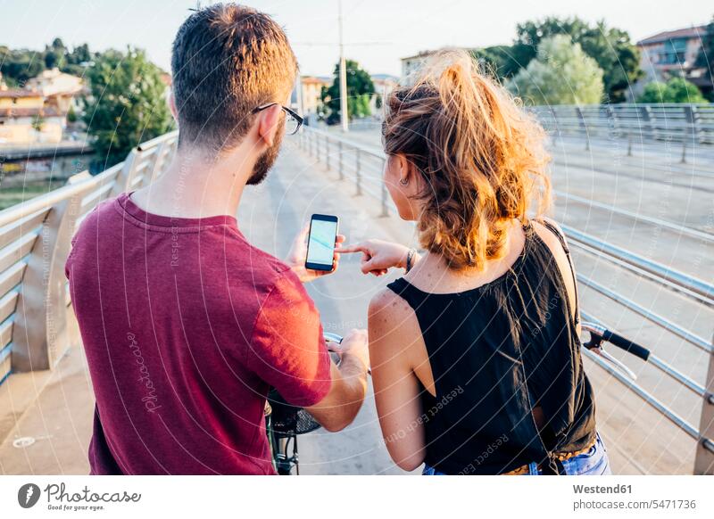 Couple using smart phone while standing with bicycles on bridge at sunset color image colour image leisure activity leisure activities free time leisure time
