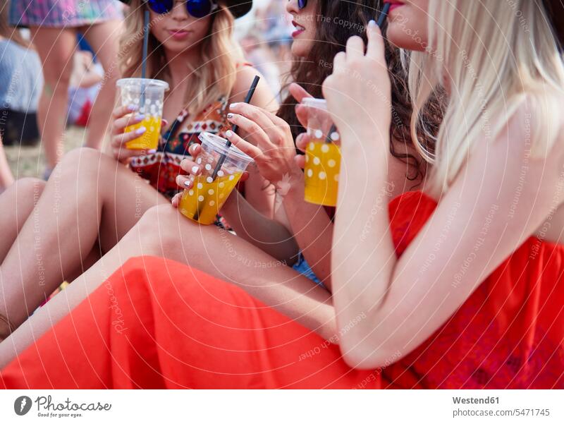 Friends drinking juice and sitting on meadow during music festival music festivals female friends woman females women Fun having fun funny celebrating celebrate