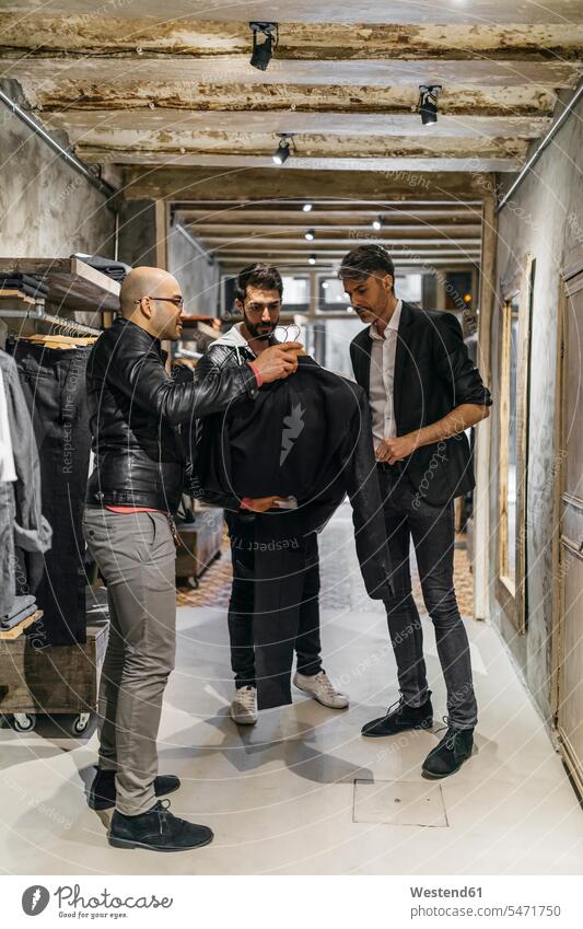 Designer and stylist in modern menswear shop offering new collection to man customer clientele clients customers Showing show men's fashion males contemporary