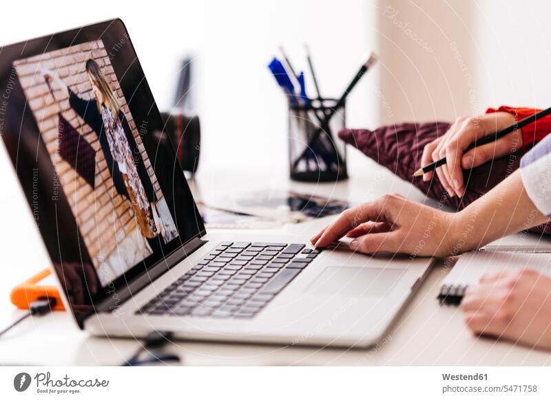 Close-up of two fashion designers working on photo on laptop photograph photographs photos woman females women fashionable female designer female designers