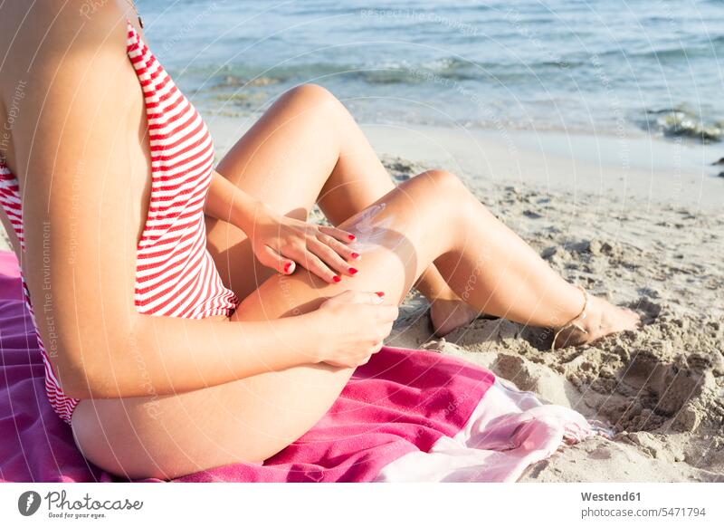 Woman sitting on the beach, putting on suncream towels swim wear bathing costume bathing costumes bathing suit bathing suits Swimming Costume Swimming Suit