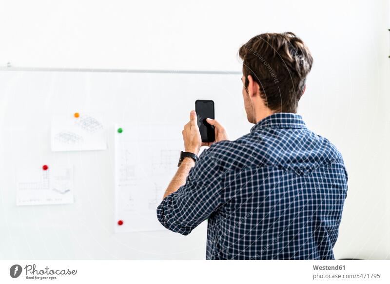 Young man taking photo of paper pin at whiteboard in office color image colour image indoors indoor shot indoor shots interior interior view Interiors day