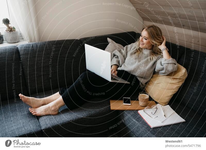 Smiling woman using laptop on sofa while freelancing at home color image colour image indoors indoor shot indoor shots interior interior view Interiors