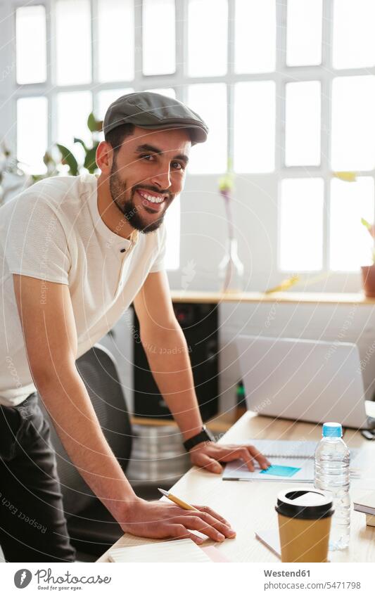 Portrait of smiling young man taking notes at desk in office making a note note taking offices office room office rooms portrait portraits desks smile workplace