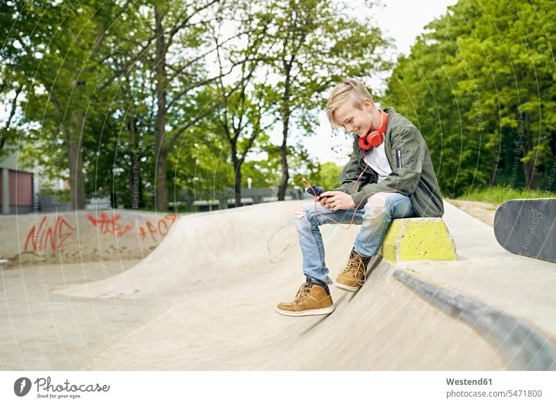 Boy with headphones in skatepark using smartphone skateboarder skater skateboarders skaters Smartphone iPhone Smartphones smiling smile cool attitude composed