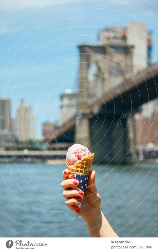 USA, New York, Brooklyn, Close up of woman hand holding a strawberry ice cream cone with Brooklyn Bridge in background Ice Cream Cone ice-cream cone