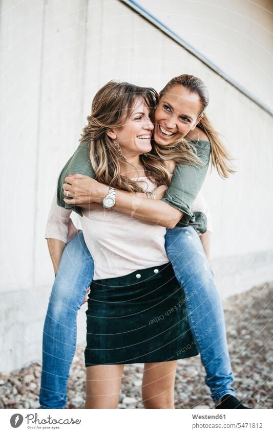 Laughing woman giving her friend a piggyback ride laughing Laughter females women friends piggy-back pickaback Piggybacking Piggy Back positive Emotion Feeling