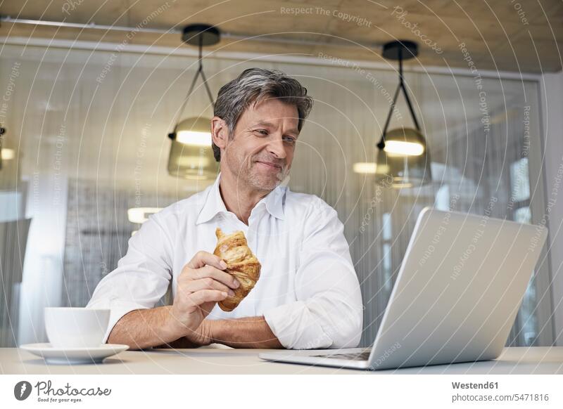 Businessman using laptop while eating croissant Laptop Computers laptops notebook Croissant Croissants Cornetto Cornettos Business man Businessmen Business men