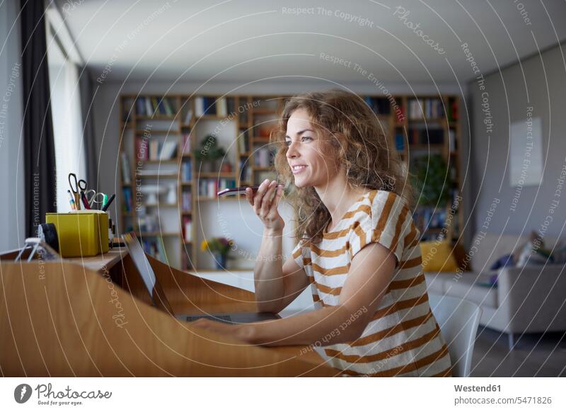 Woman talking on mobile phone while sitting by desk at home color image colour image indoors indoor shot indoor shots interior interior view Interiors day