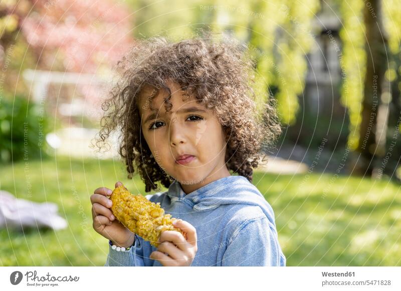 Portrait of boy eating a corn cob in garden human human being human beings humans person persons curl curled curls curly hair hold summer time summertime