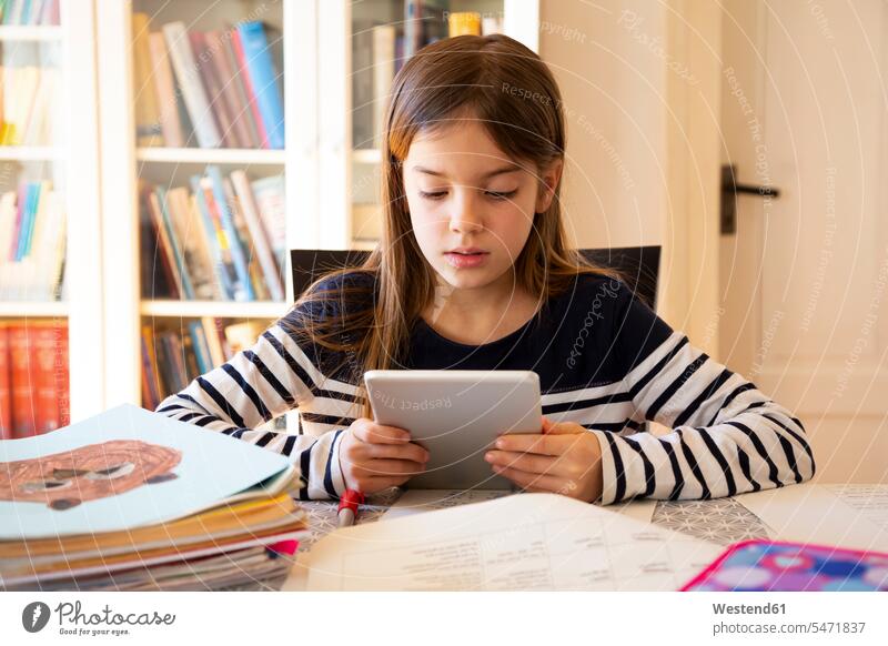 Girl doing homework with digital tablet rack racks Shelve shelves book shelf Book Shelves bookshelves Tables pencil pencils pens learn read Seated sit at home