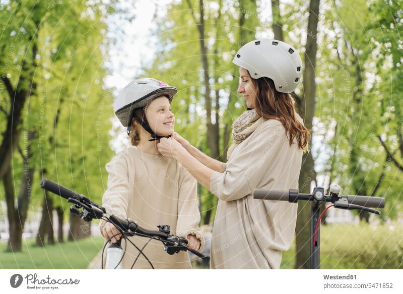 Mother wearing helmet to her daughter against trees in city park color image colour image leisure activity leisure activities free time leisure time