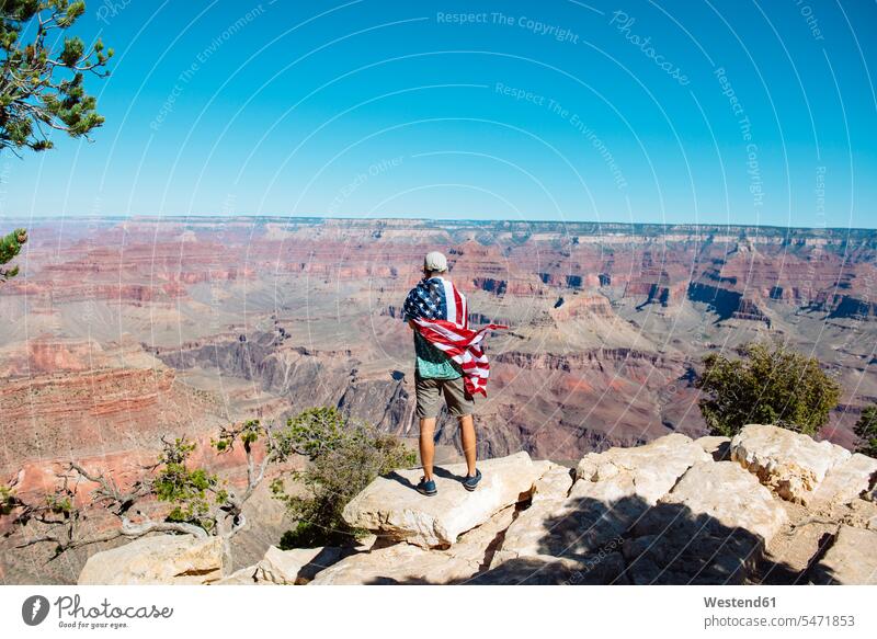 USA, Arizona, back view of man wrapped in American flag enjoying view of Grand Canyon National Park indulgence enjoyment savoring indulging View Vista Look-Out