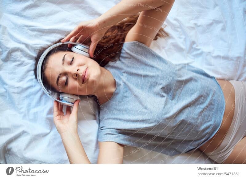 Portrait of young woman with eyes closed lying on bed listening music with headphones human human being human beings humans person persons caucasian appearance