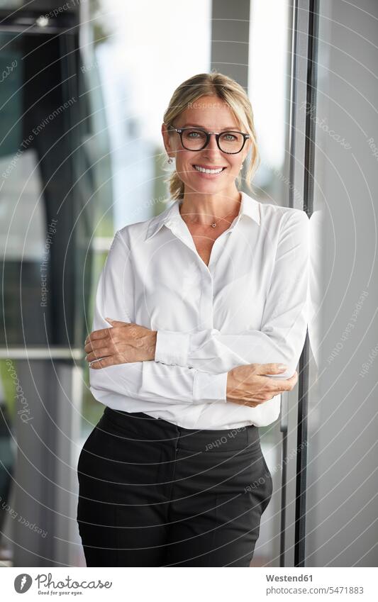 Businesswoman in office leaning against window, with arms crossed glass pane glass panes portrait portraits Arms Folded Folded Arms Crossed Arms Crossing Arms