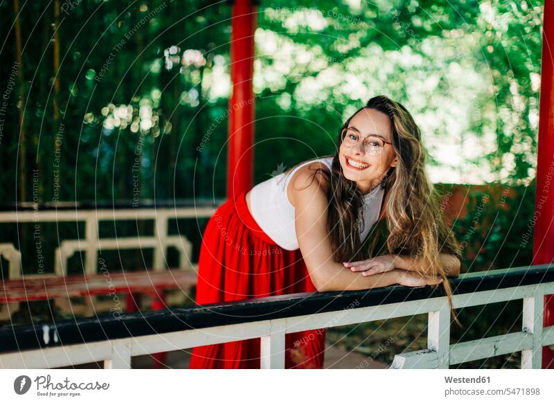 Smiling young woman with long hair standing by railing on footbridge in park color image colour image Portugal leisure activity leisure activities free time