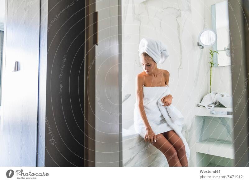 Woman wrapped in towels, sitting on edge of bathtub Wrapped in a towel woman females women tubs bathtubs bath tubs Bath turban Turbans Seated Adults grown-ups